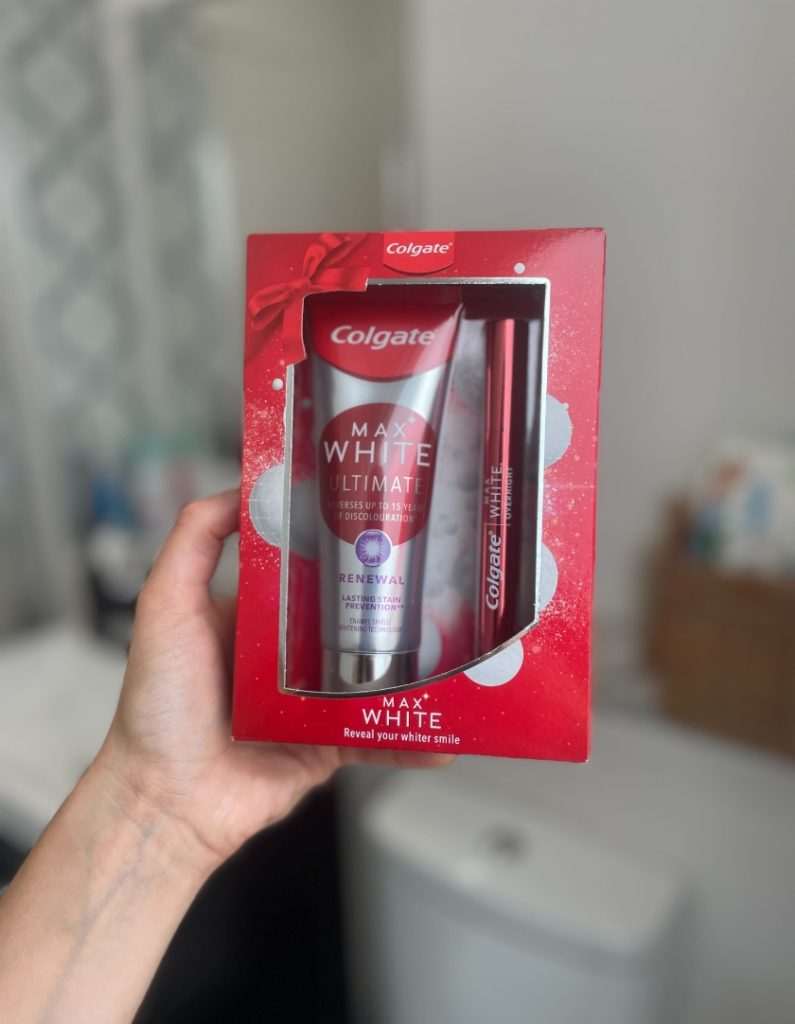 Shows the hand of a consumer holding a box Colgate Max White during a home sampling activation