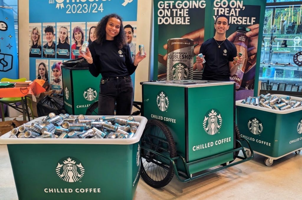 Two promotional workers holding Starbucks samples in a university foyer