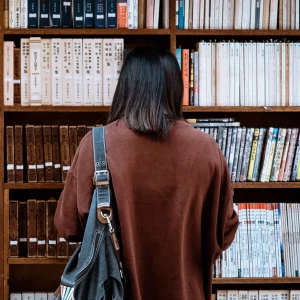 Shows a lady in University looking at books in a library